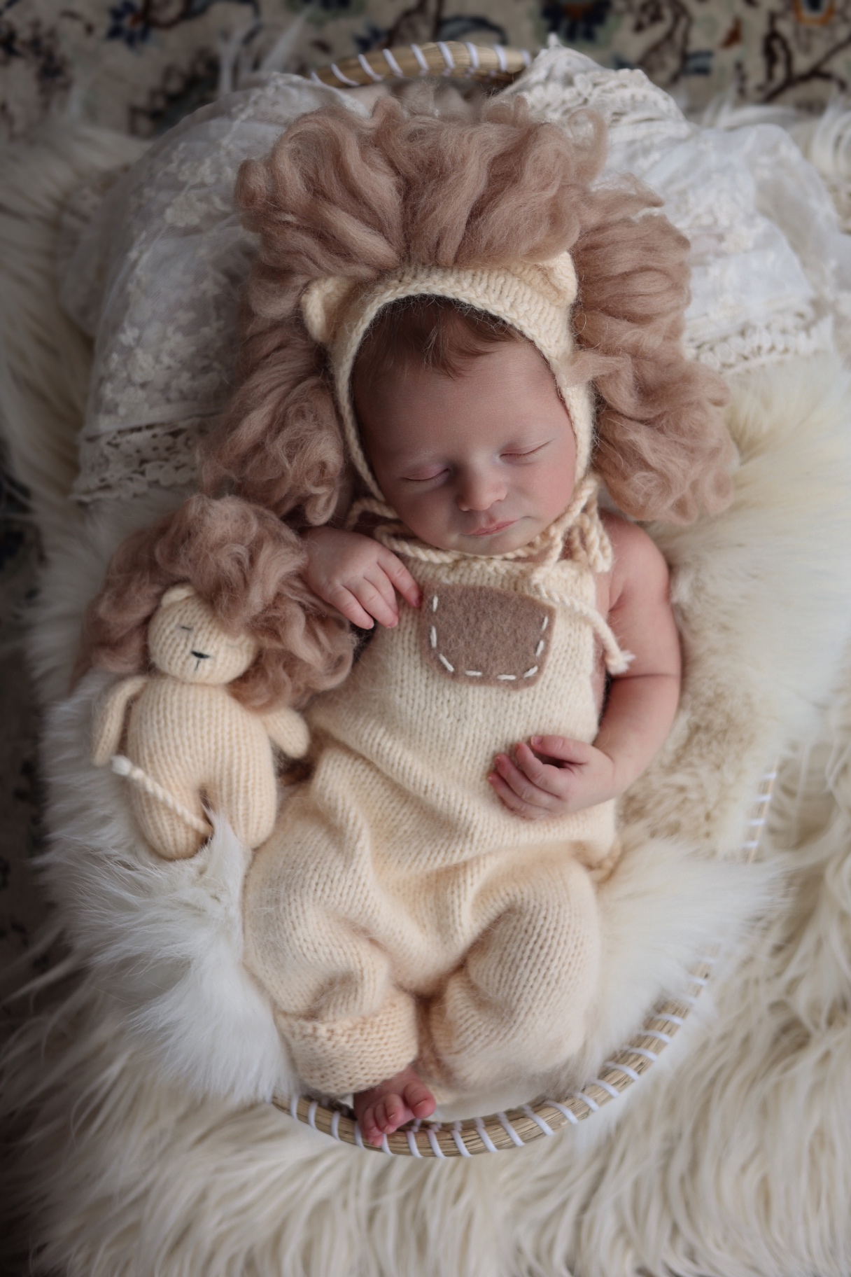 Newborn in a knitted lion outfit cuddling a tiny lion toy