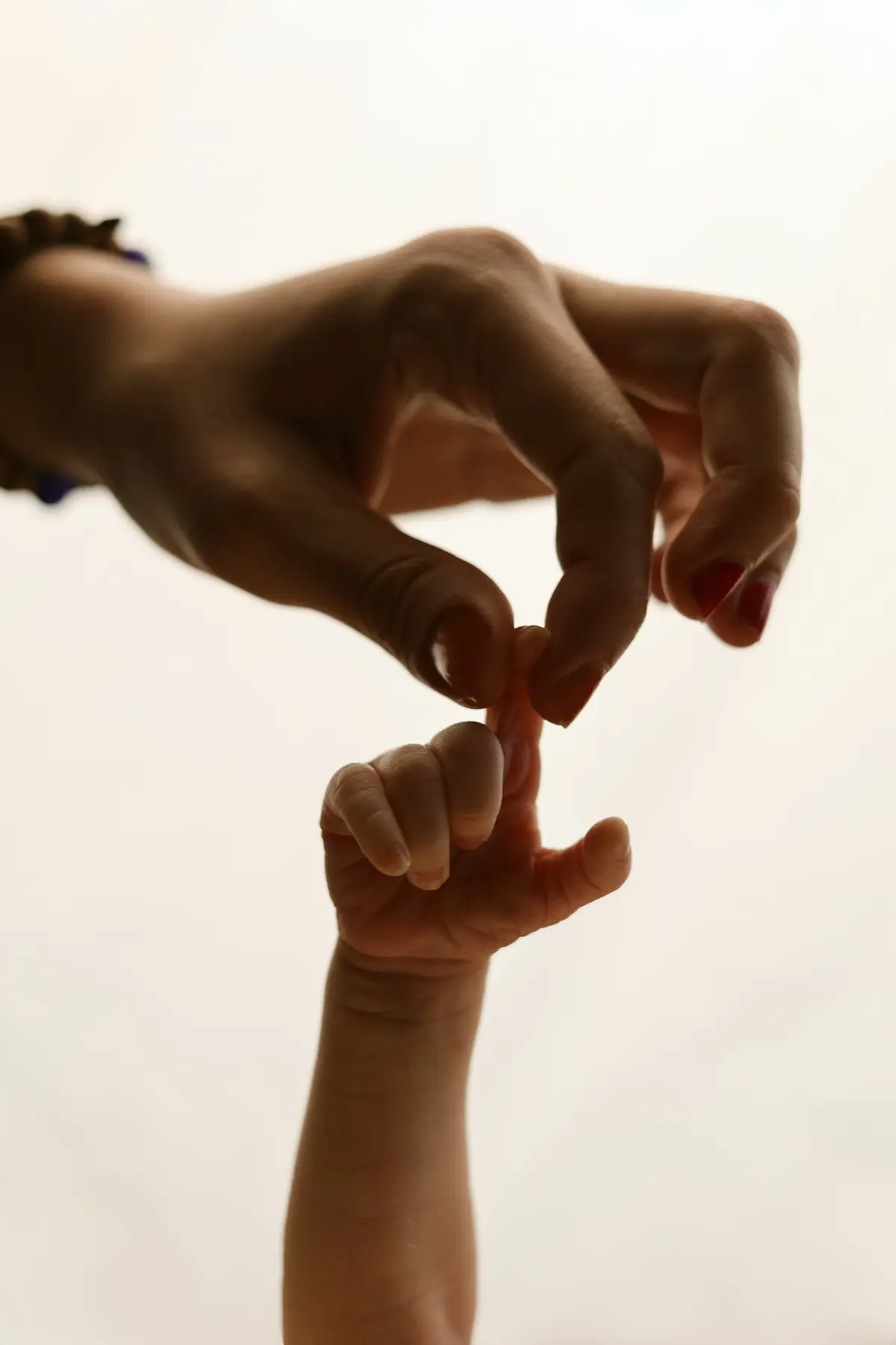 Newborn hand holding mother's finger against a warm cream background