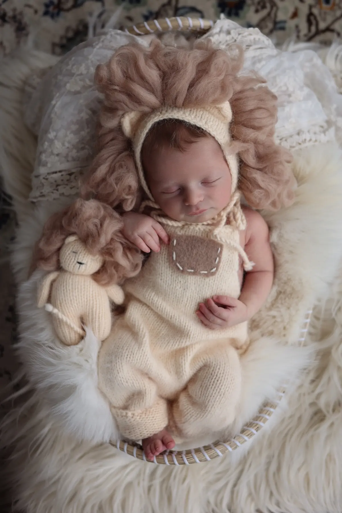Newborn in a knitted lion outfit cuddling a tiny lion toy
