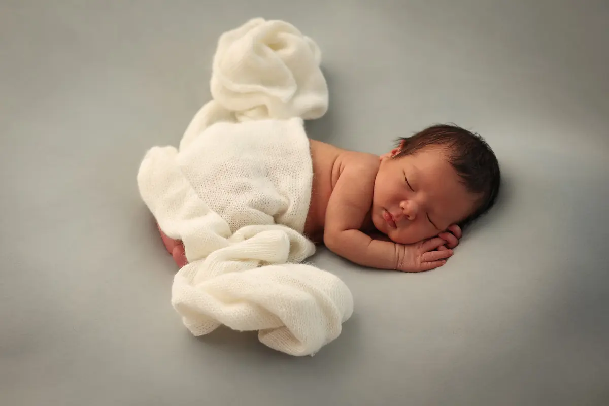 Sleeping newborn wrapped in a soft cream knit on a grey backdrop