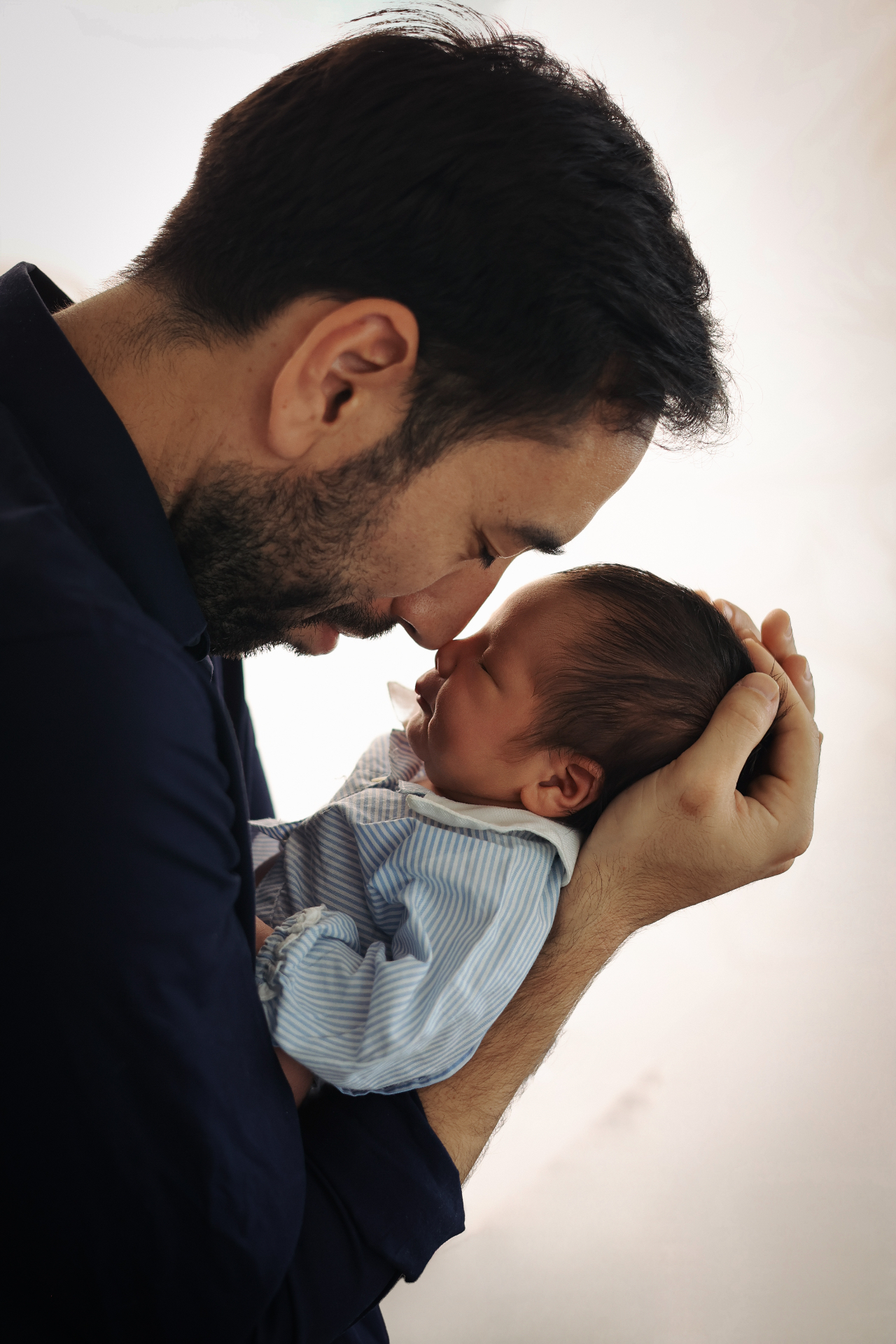 Father touching foreheads with his newborn baby in soft backlight